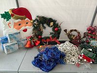 Photo showing Santa face decoration, blue tinsel garland, green wreath with ornaments, and LED light boxes.