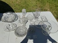 Top view of clear glassware on white table including bowls, pie stand, flower holders, vases, and small dishes.