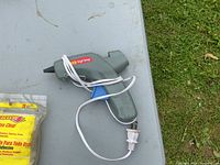 Light gray hot melt glue gun with a power cord wrapped around it and blue stand on a gray surface