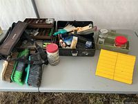 Two tackle boxes filled with assorted nails, screws, brushes, and miscellaneous hardware items on a table.