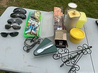 Full lot overview on a folding table outdoors, showing sunglasses, Tupperware, hooks, locks, and other small household items.