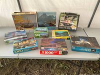 Photo showing all nine puzzle boxes arranged on a table outdoors. Boxes display variety in puzzle image themes and piece counts.