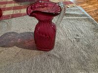 Side-angle view of cranberry art glass pitcher showing quilted texture and clear handle