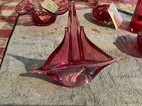 Image showing pink glass sailboat sculpture from a side view, highlighting curved sails and base.