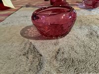 Side view of the small cranberry glass sugar bowl showing its rounded shape and textured pattern on a neutral surface.