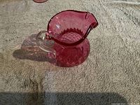 Side angle view of small deep pink glass pitcher with clear handle