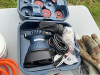 Mastercraft palm sander inside molded plastic carrying case with sanding discs and dust bag, and work gloves beside it.