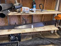 Shelf with two large dual-handed crosscut saws lying flat, showing full blade length with teeth and wooden handles on each end.