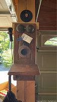 Front view of an antique wooden wall-mounted telephone showing two metal bells, a mouthpiece, and a wooden shelf.
