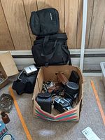 Full view of box containing cameras and accessories, including camera carrying cases and Kodak camera in brown case.