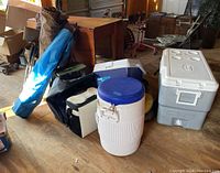 Photo showing coolers in various sizes and colors, along with insulated beverage container and camping chairs in bags.