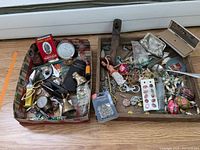 Photo showing the entire lot with assorted costume jewelry, miniatures, pocket cutlery, and small decorative items placed inside two holiday-themed boxes.