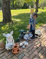 Photo of assorted outdoor garden decorations on a brick patio with grass and trees in background.