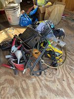 Overview of assorted hand saws, jumper cables, electrical cords, funnels, clamps, and other assorted hardware and tools on plywood floor in garage.