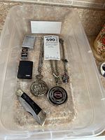 Overhead photo of all items in clear container, showing watches, chains, skull necklace, lighters, and pocket cutter