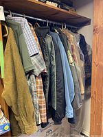 Photo showing a variety of hanging men's and women's clothing items on a metal rod rack, shows jackets, shirts, and coats in various materials and colors.