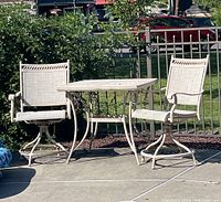 Photo showing entire outdoor bistro set with table and two swivel rocking chairs on a patio with greenery and fence in background.