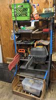 Full view of black metal shelving loaded with chainsaws, tools, and storage crates