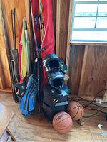 Wide view showing assortment of fishing poles, bags, two basketballs, and helmets in wooden room corner.