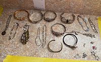 Full view of all 15 sterling silver bracelets and charms displayed on a beige mottled surface showing different styles and sizes.