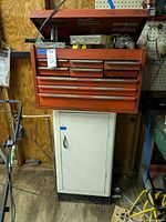 Front view of orange metal toolbox with multiple drawers mounted above white metal cabinet in shed.