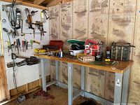 Overview of workbench with assorted hand tools and supplies arranged on bench surface and pegboard behind.