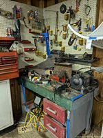 Overview of workbench showing bench grinder, vise, clamps, various small tools, red drawers, and an industrial lamp above the bench.