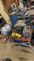 Table with various power tools and battery chargers including Sear battery charger, Battery Tender charger, DeWalt tool case, cords and other tools untested and dusty.
