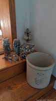Photo showing the Western Stoneware crock, clear glass oil lamp, two jars of marbles, a square glass container of marbles, and several miniature figurines on wooden stairs.