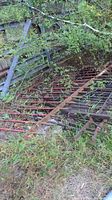 Four sections of wrought iron fencing lying outdoors over grass and near plants, showing rust and weathering.