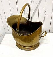 Side view of antique copper coal scuttle showing curved large body, thick top handle, and side carrying handle with natural wear and patina.