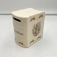 Front and side view of the Bunnykins ceramic book bank showing the slot on top and Bunnykins illustrations of rabbits.