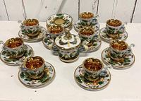 Full set arranged showing sugar bowl in center surrounded by nine demitasse cups on twelve saucers, showcasing hand-painted raised cherubs, dragon handles, and gold accents.