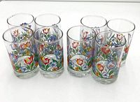 Eight clear cylindrical juice glasses displayed together, each decorated with colorful tulip and floral designs around the bottom half.