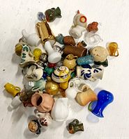 Top view of mixed miniature jugs, urns, and mugs in various materials and colors on white surface.