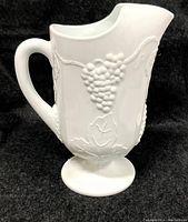 Front and side profile of white milk glass pitcher showing raised relief grape clusters and vine leaves.