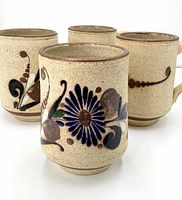 Front view showing four large Mexican pottery mugs with hand-painted floral designs on speckled beige background.