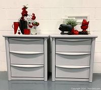 Pair of soft dove grey bedside tables each with three drawers, styled with red and black decorative items on top.
