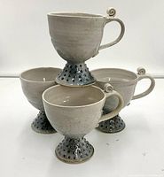 Four pedestal pottery mugs arranged showing the raised dotted bases and curled scroll handles.