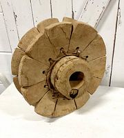 Side view of the vintage wood and leather Bakra pulley, showing weathered wood, leather strappings, and central hollow cylinder.