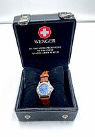 Front view of Wenger Swiss Ladies watch on black cushion inside black box with Wenger logo and slogan.