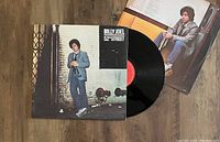 Vinyl record partially out of cover with inner sleeve visible, showing album cover art and vinyl disc with label.