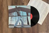 Photo showing Billy Joel Glass Houses LP vinyl record with album cover and lyric inner sleeve on a wooden surface.