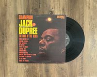 Vinyl LP record and sleeve of Champion Jack Dupree The Best Of The Blues laid flat on wood surface with record partially out of sleeve