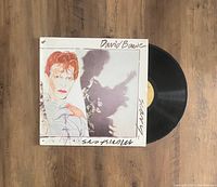 David Bowie Scary Monsters vinyl LP partially out of sleeve on wooden floor, showing cover art and record.