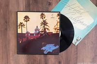 Photo showing the Eagles Hotel California UK 1st pressing LP vinyl record partially removed from its iconic picture sleeve with the album inner sleeve also visible.