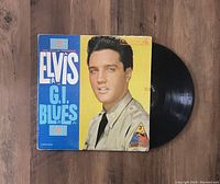 Vinyl LP record partially out of its colorful original cover featuring a close-up of Elvis Presley in uniform for the G.I. Blues album.
