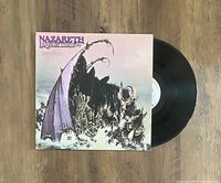 Vinyl record and album cover with demonic creatures artwork visible, showing record partially pulled out of sleeve on wooden floor.