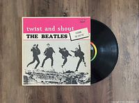 Photo showing black vinyl record partially out of cover and front cover of The Beatles Twist and Shout album with the band jumping in black and white photo