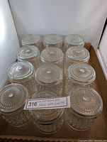 12 clear pressed glass light globes arranged in a box, showing various embossed geometric and sunburst patterns on top and sides.